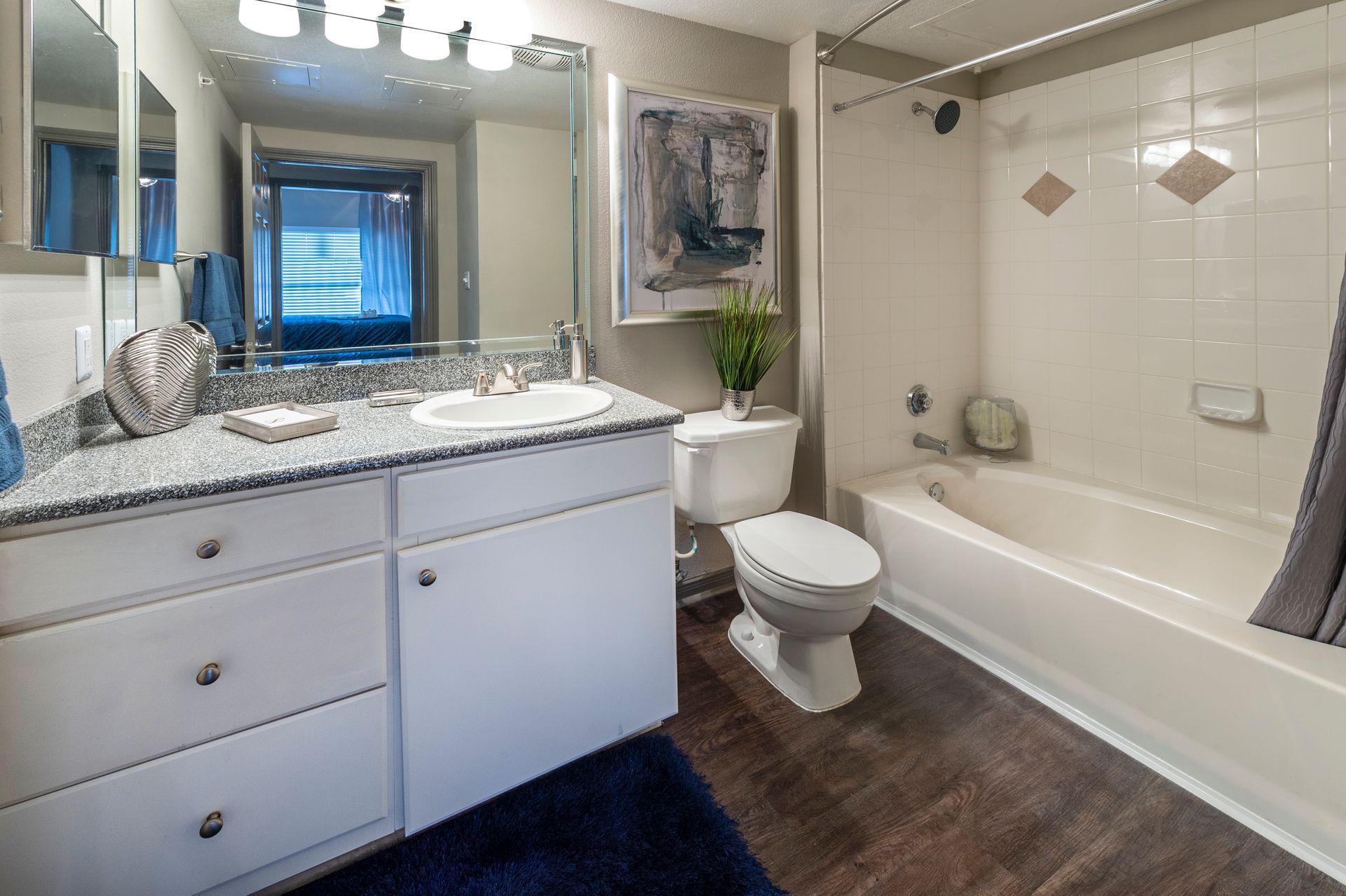 A bright bathroom with white vanity cabinets, granite countertop, toilet, and a white tiled shower-tub combo at Lexington at Champions in Houston, TX..