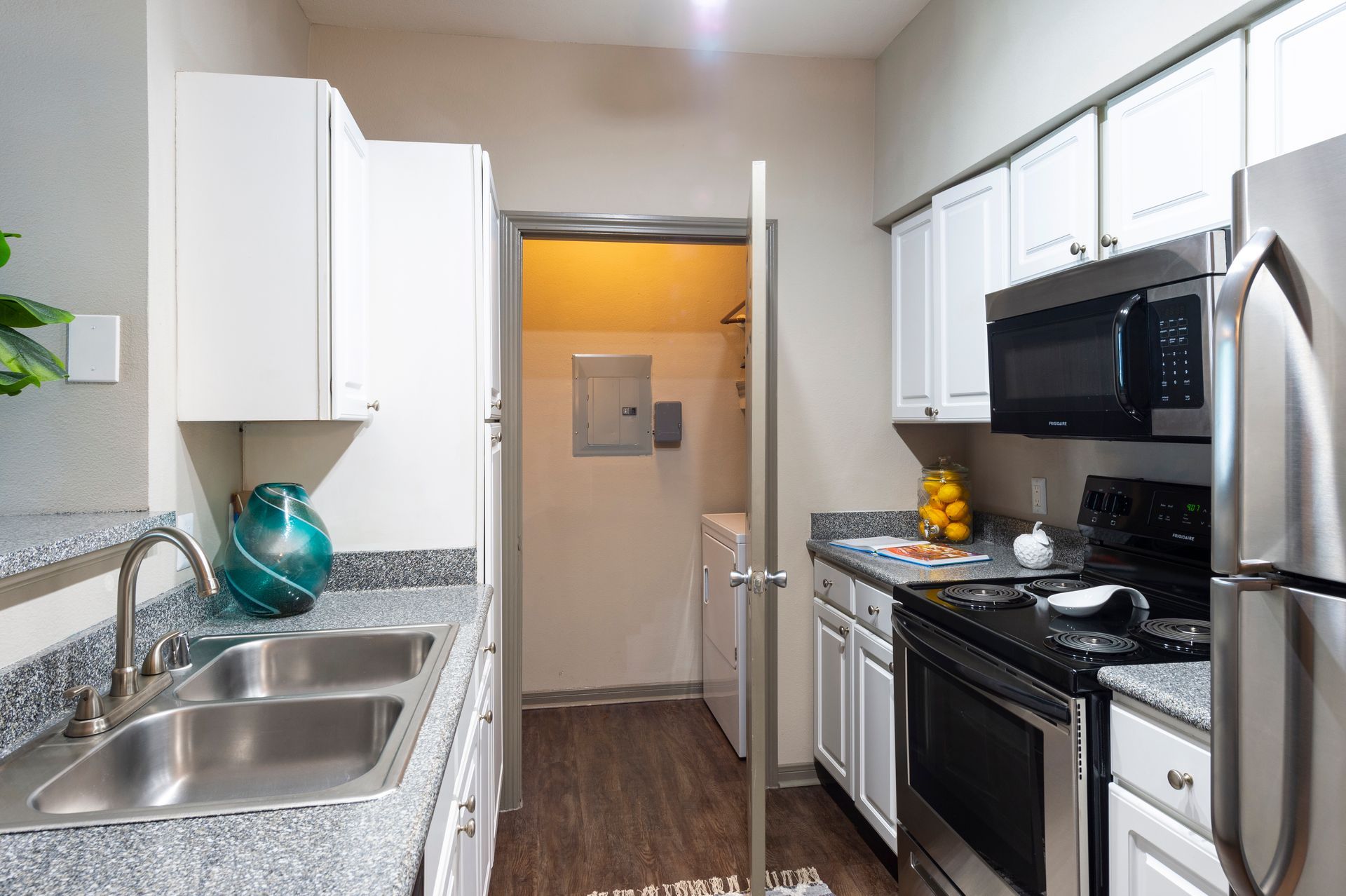 A kitchen with granite countertops, stainless steel appliances, white cabinets, and a doorway leading to a laundry area at Lexington at Champions in Houston, TX..