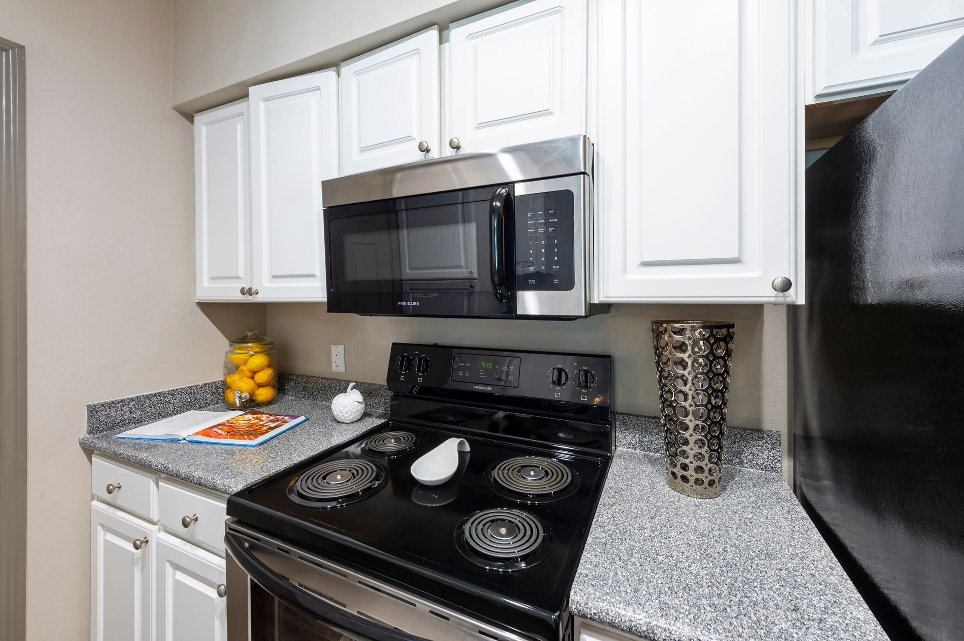 A kitchen corner featuring white cabinets, a stainless steel microwave, a black stove, and granite countertops at Lexington at Champions in Houston, TX..
