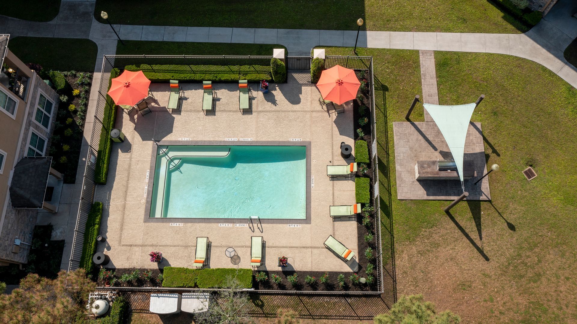 Aerial view of an apartment swimming pool area featuring loungers, two orange umbrellas, and a shaded seating section at Lexington at Champions in Houston, TX..
