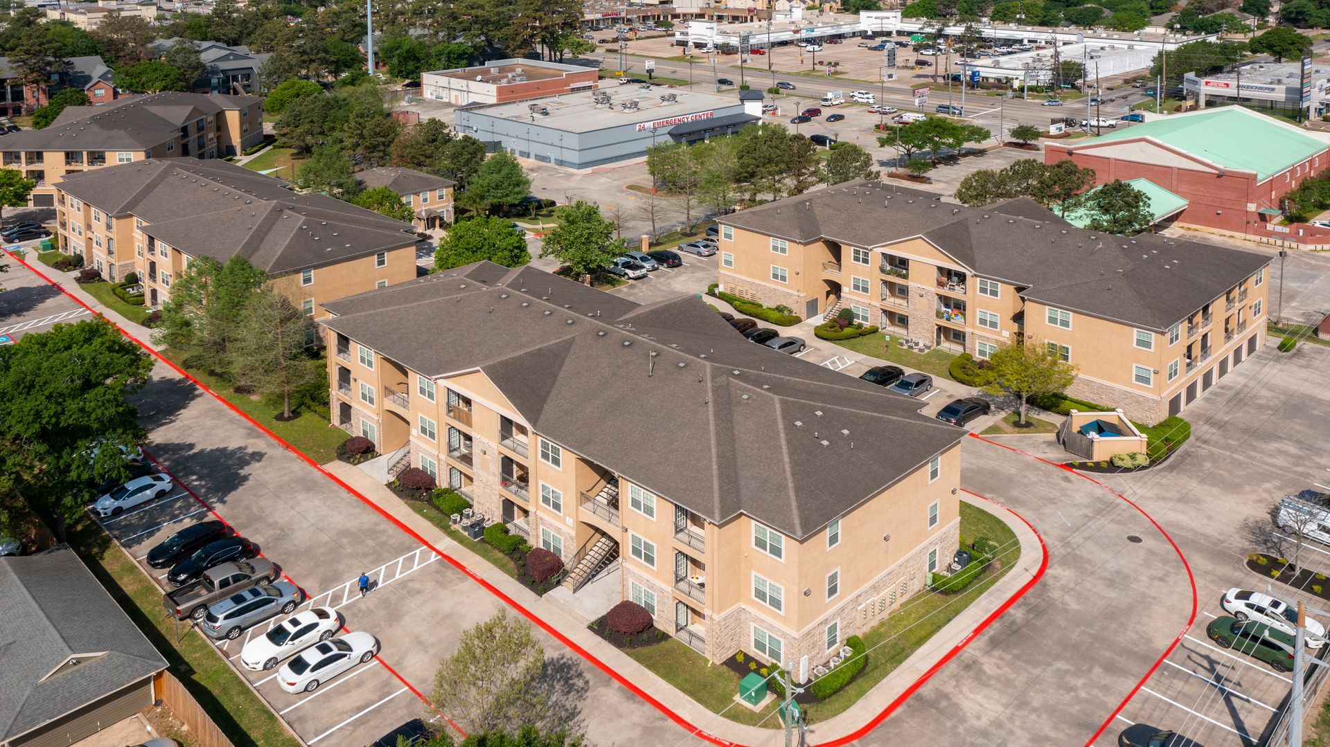 Aerial view of multi-story apartment buildings with parking, near a city setting.