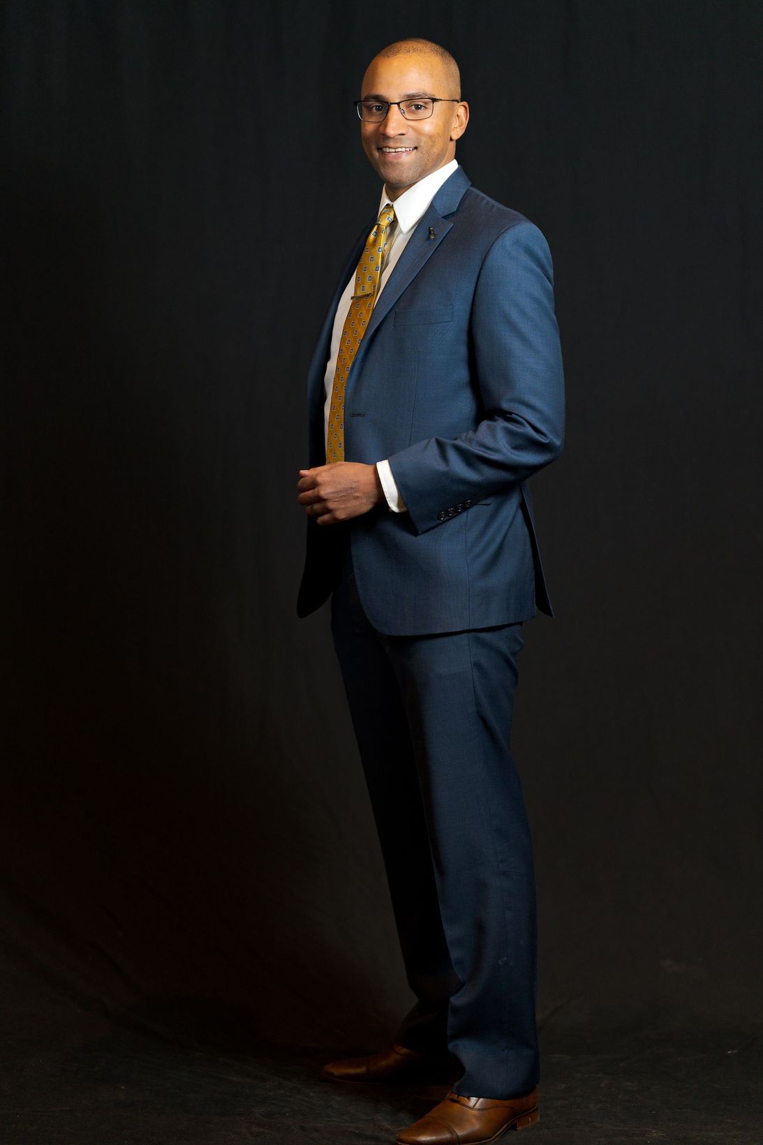 Full length professional photo of Jevon Gondwe wearing full blue suit with orange tie