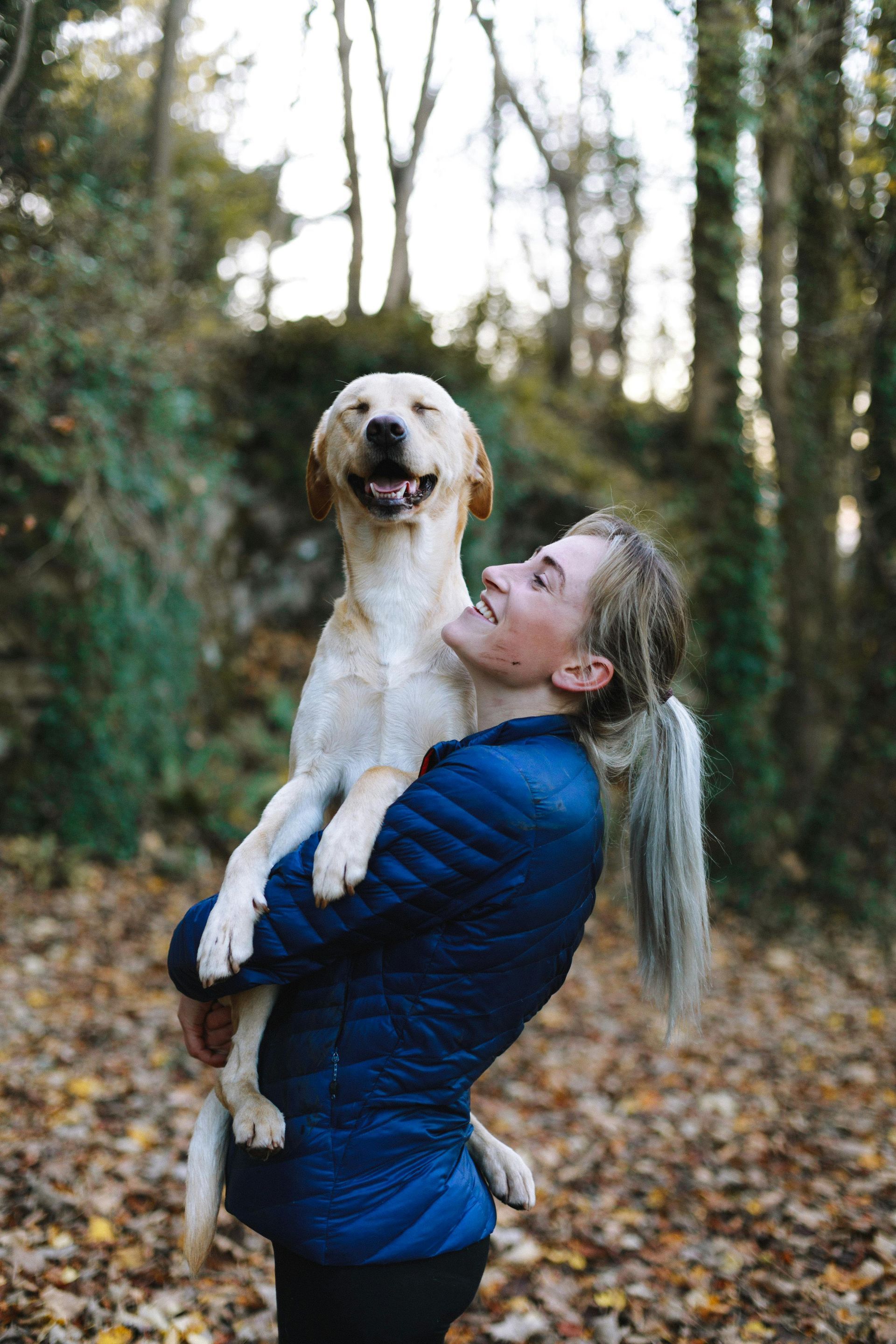 A woman is holding a dog in her arms in the woods.