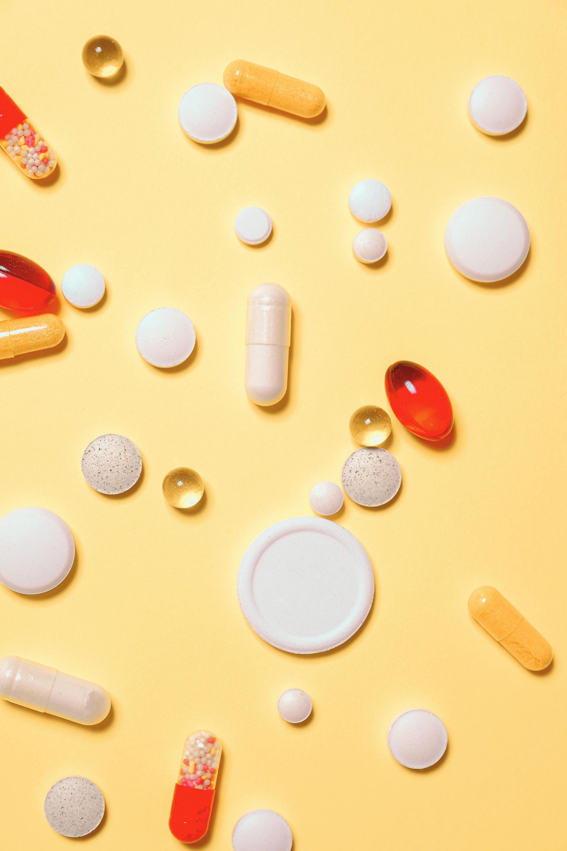There are many different types of pills and capsules on a yellow background.