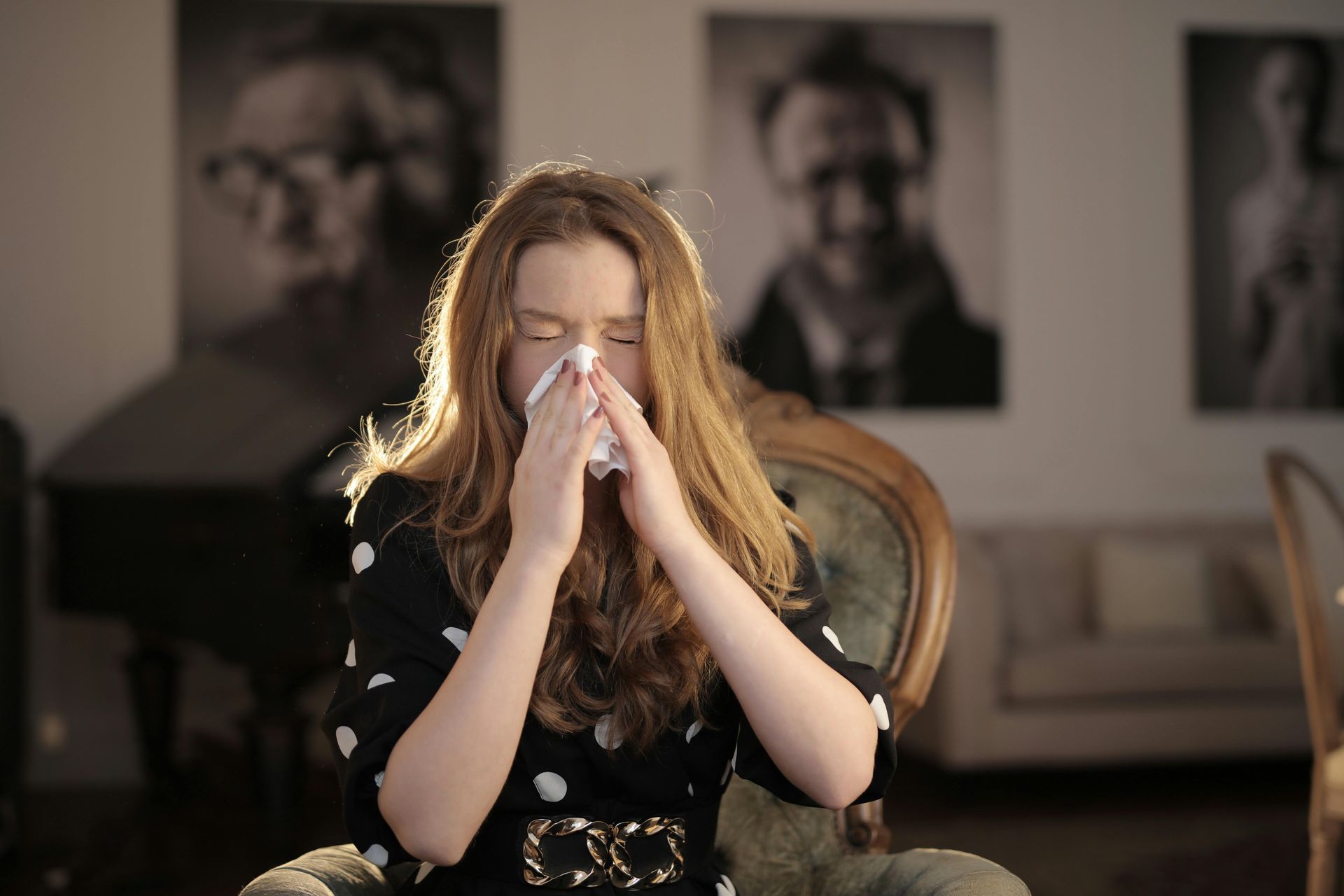 A woman is blowing her nose into a napkin while sitting in a chair.