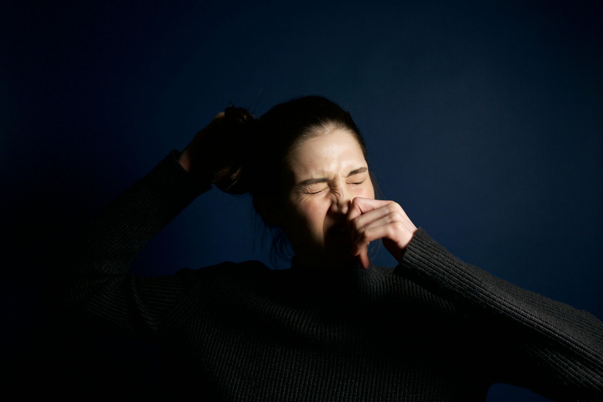 A woman is covering her nose with her hand in the dark.