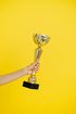 A hand is holding a gold trophy on a yellow background.