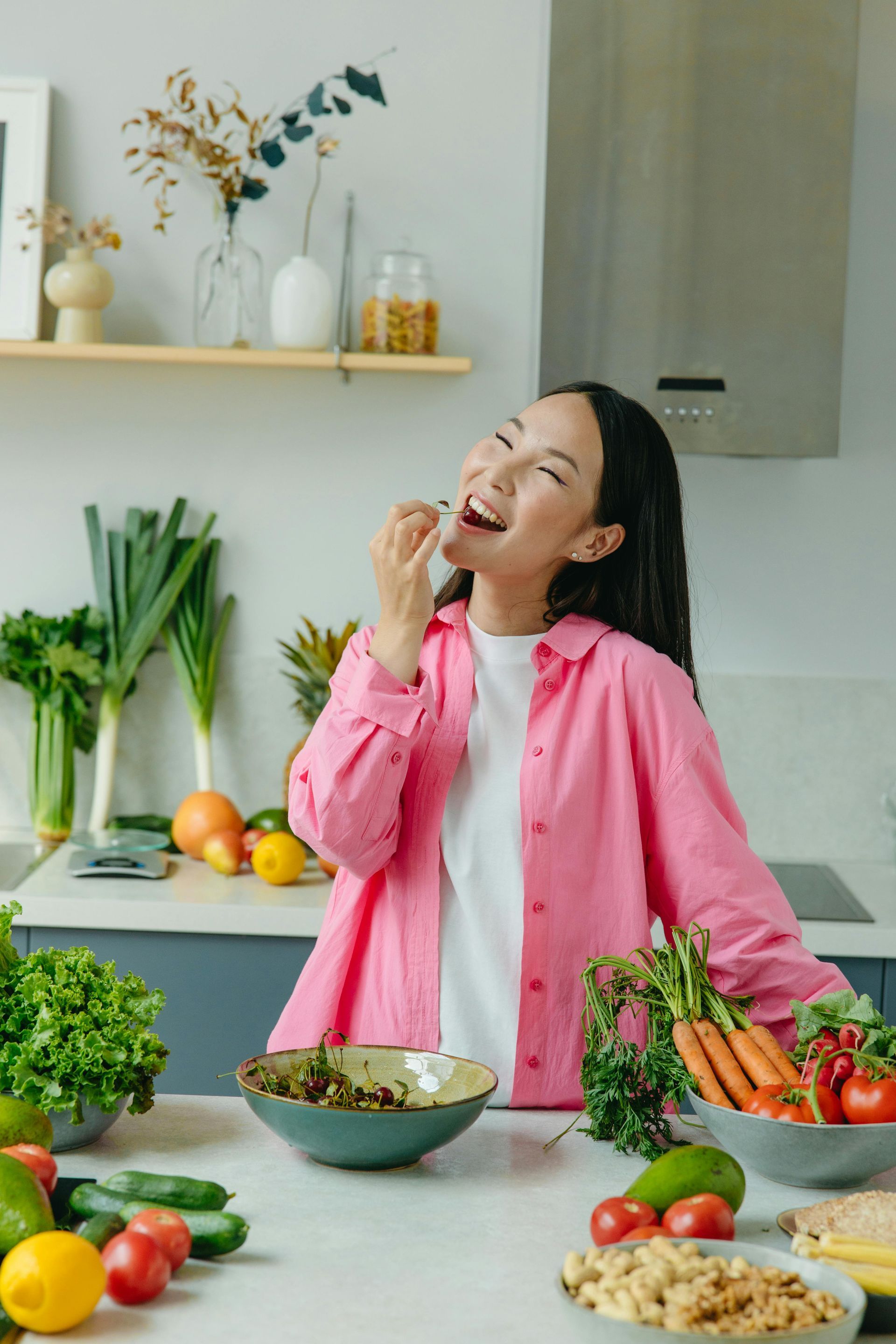 A woman in a pink shirt is eating a salad in a kitchen.