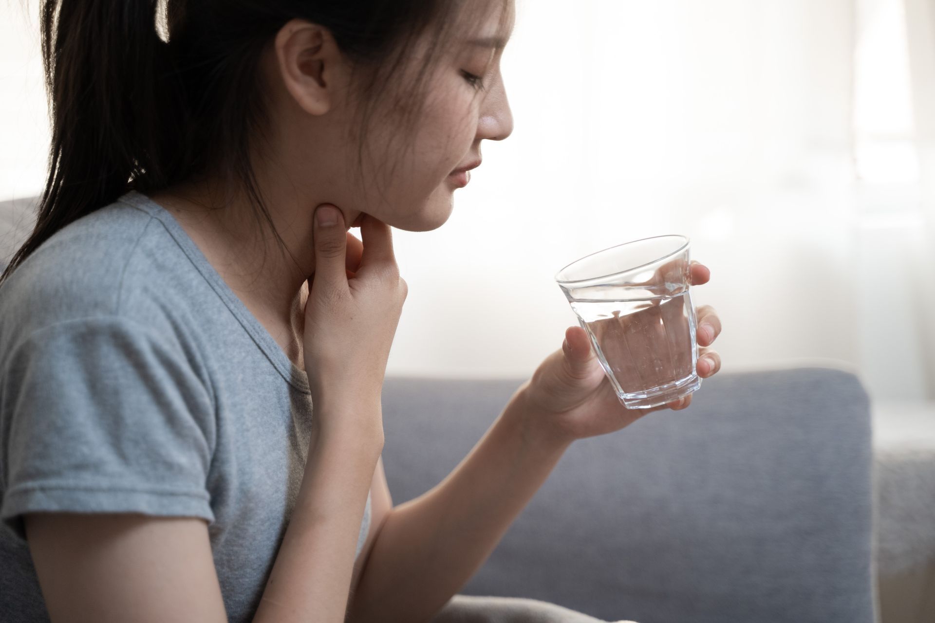 A woman is sitting on a couch holding a glass of water.
