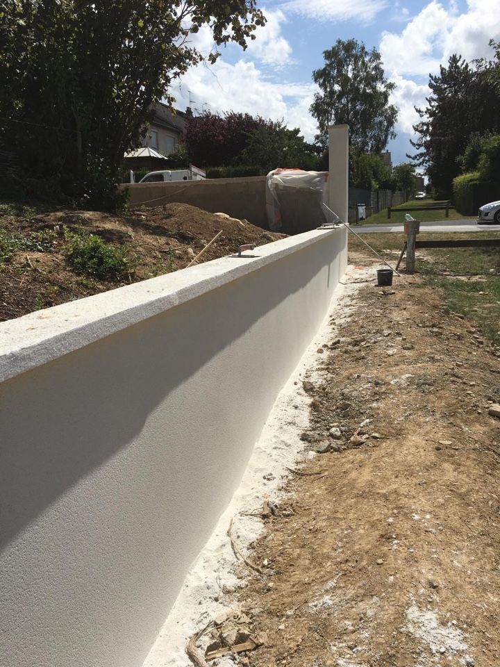 Un mur blanc est en train d’être construit au milieu d’un champ de terre.