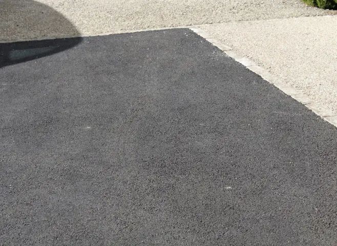 Une allée en asphalte noir menant à une porte de garage.