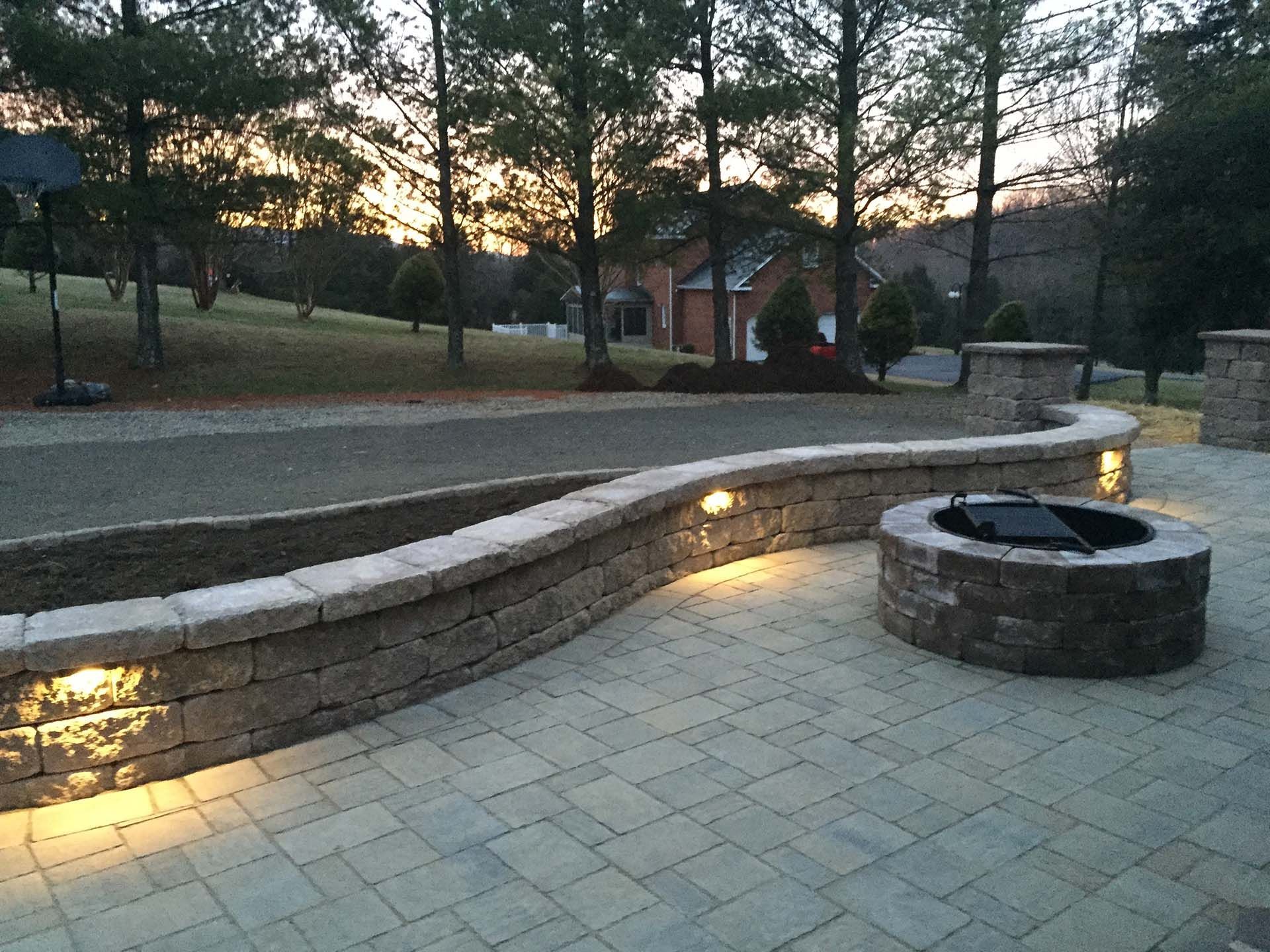 A fire pit in the middle of a brick patio with lighting