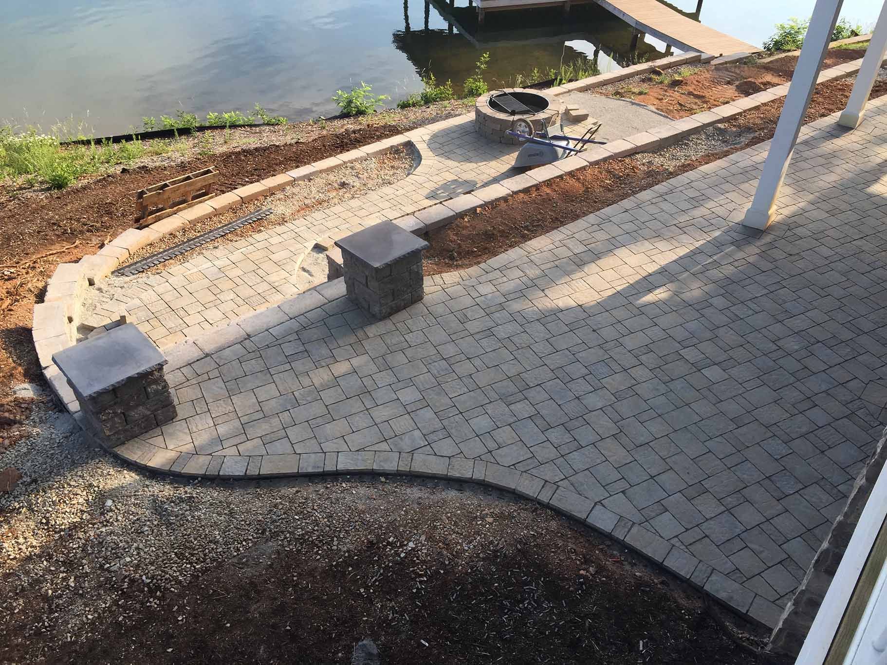 A patio with a fire pit and a dock next to a body of water