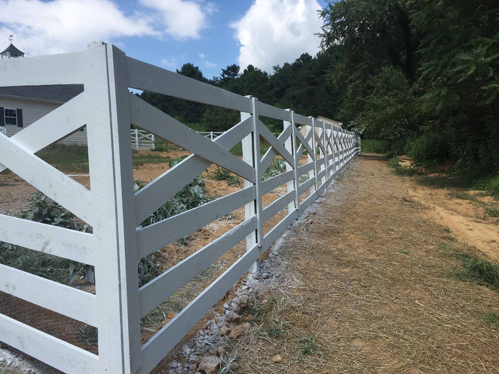 A white fence along a road with trees in the background