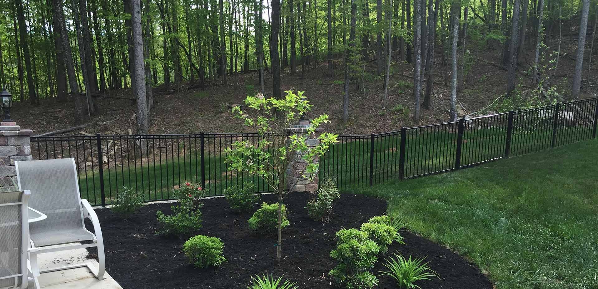 A backyard with a fence, chairs, and trees