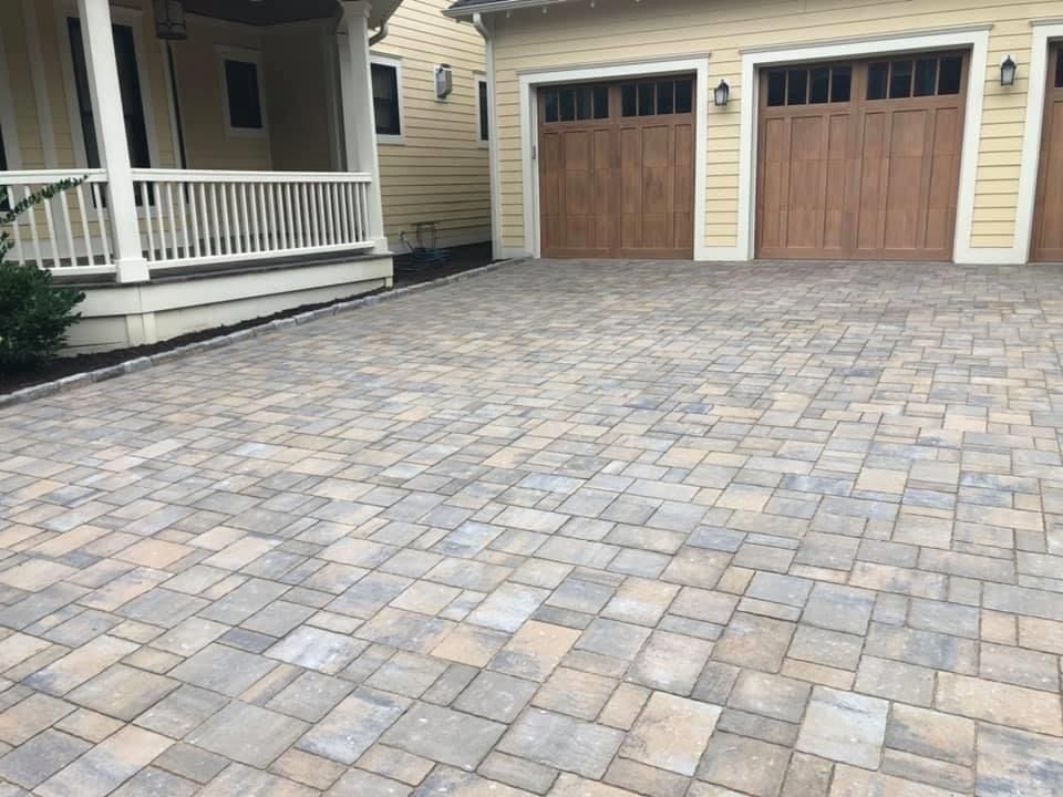 A brick driveway in front of a house with two garage doors