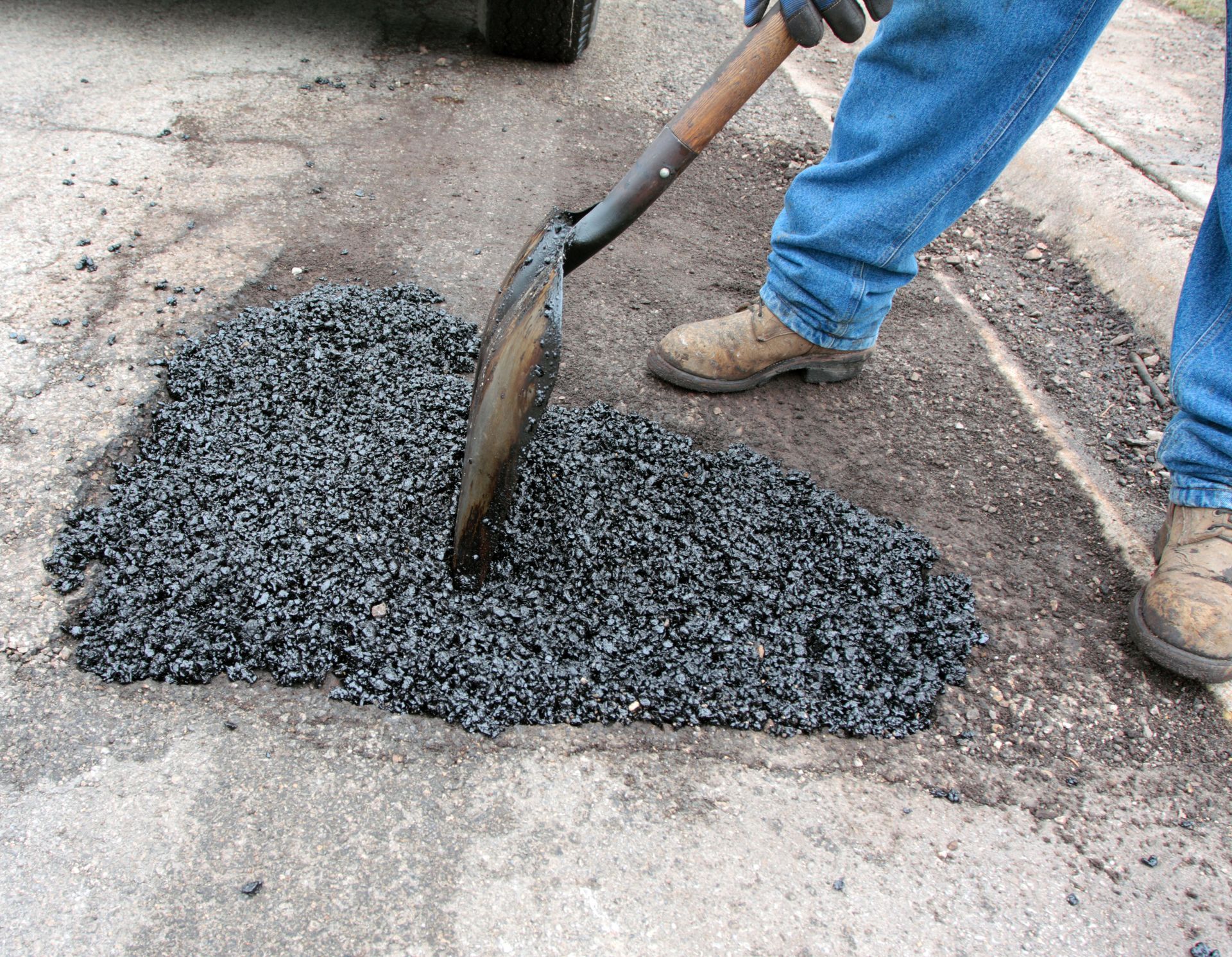 A contractor performing road patching services, by filling a pothole with hot mix asphalt.