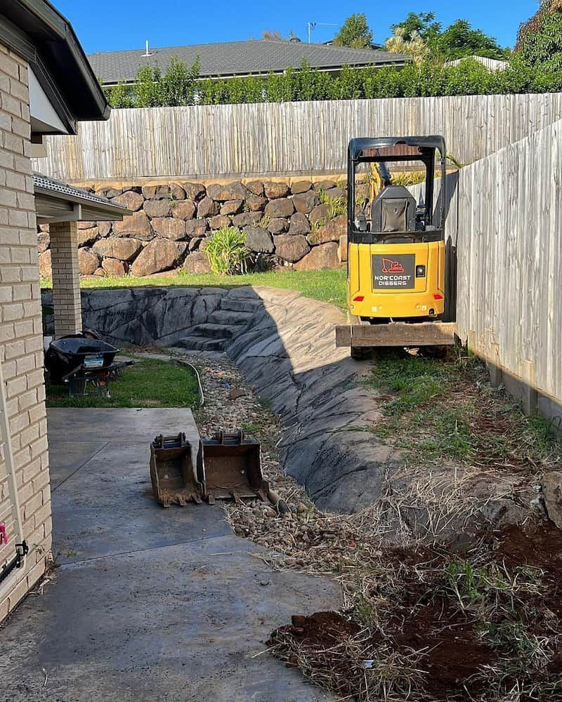 A Yellow Excavator is Parked in the Backyard of a House — Norcoast Diggers in Ballina, NSW