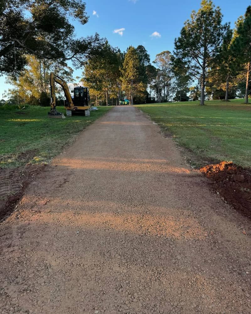 A Dirt Road With a Yellow Excavator on the Side of It — Norcoast Diggers in Byron Bay, NSW