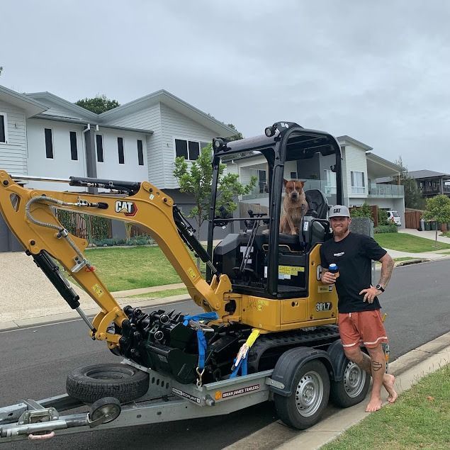 A Man and a Dog Are Standing Next to a Cat Excavator on a Trailer — Norcoast Diggers in Ballina, NSW