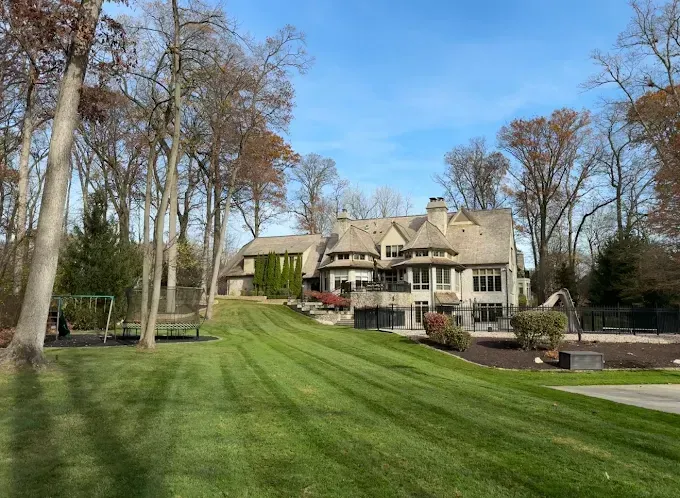 Large house with a manicured lawn, surrounded by trees under a blue sky.