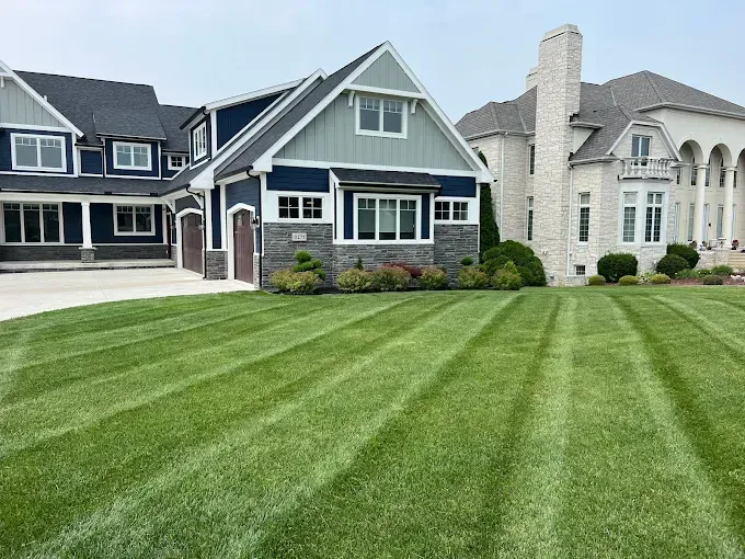 Well-manicured lawn with striped patterns in front of two large, upscale houses.