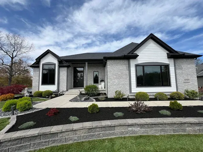 Gray brick and white siding house with black trim, manicured lawn, and cloudy sky.