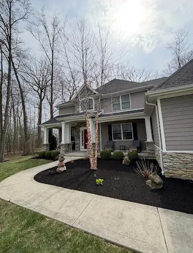 Two-story gray house with white pillars, a porch, and black mulch in the yard. A sidewalk curves toward the front door.
