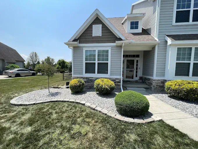 Front of a gray house with landscaping, blue sky. A sidewalk leads to the front door.