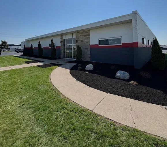 Exterior of a building with a gray and red color scheme, arched walkway, green grass, and shrubs.