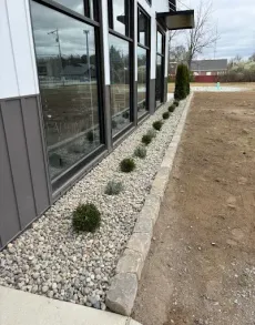 Gray concrete bollard border around a green lawn and brick patio.