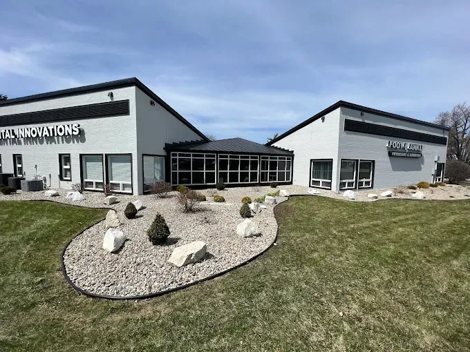 Two-story gray building with a landscaped yard, under a blue sky.