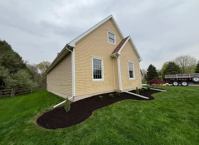 Yellow house with dark mulch border, two windows, green grass, and overcast sky.