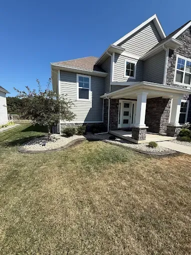 Two-story house with gray siding and stone accents, blue sky, dry lawn.