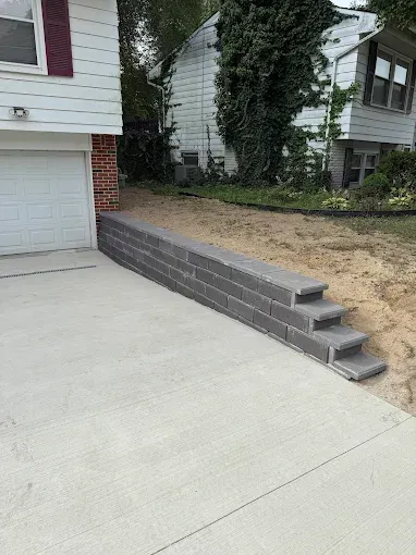 Concrete block retaining wall with steps next to a driveway in front of a house.