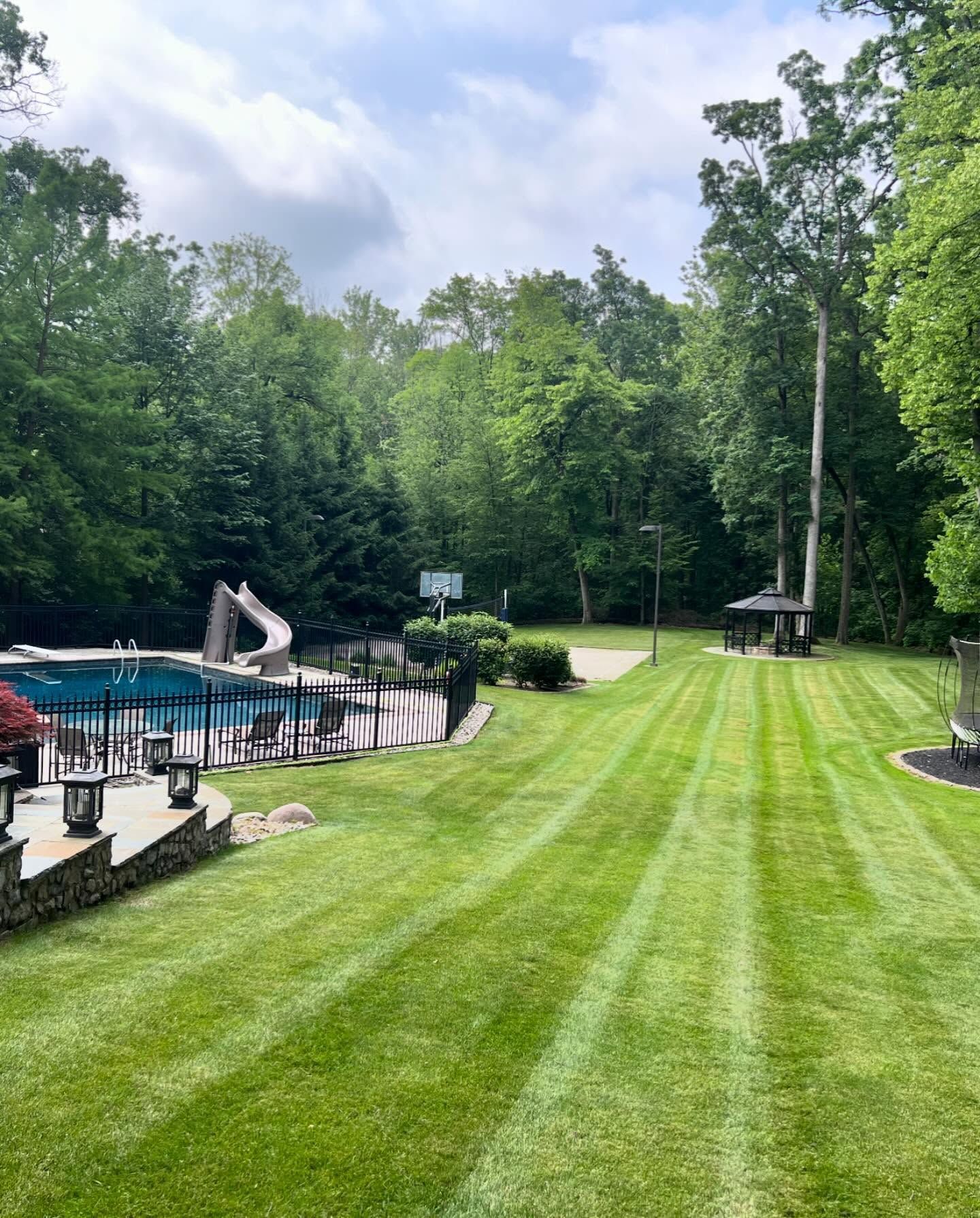 Green lawn with swimming pool and trees under a cloudy sky.