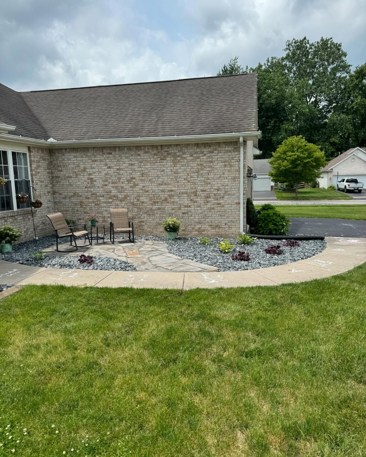 A house with a patio seating area, surrounded by landscaping and a curved walkway.