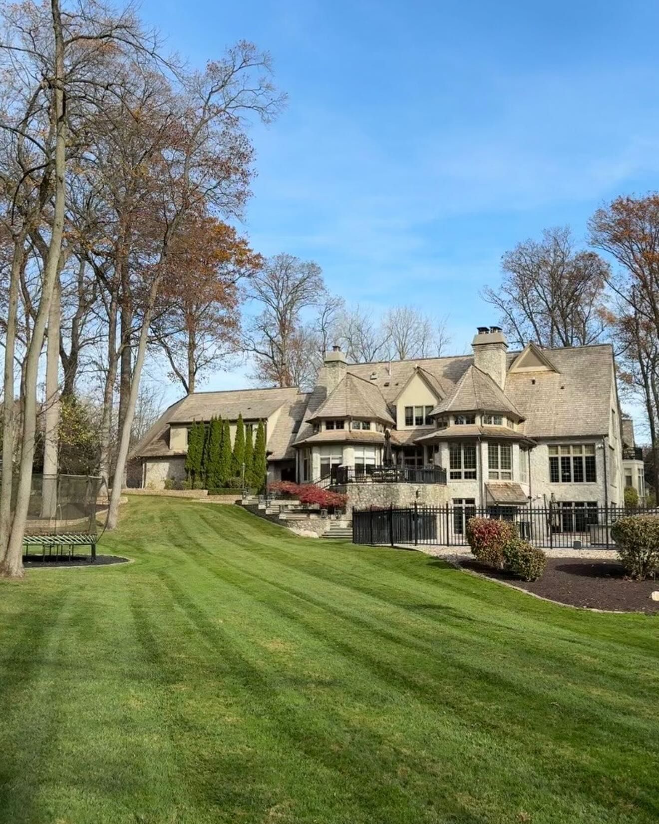 Large house with manicured lawn, trees, and a blue sky.