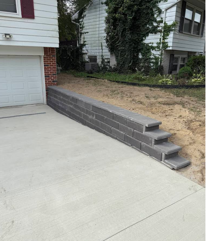 Gray block retaining wall with steps alongside a concrete driveway.