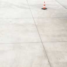 Orange and white traffic cone on a light-colored concrete surface with seam lines.