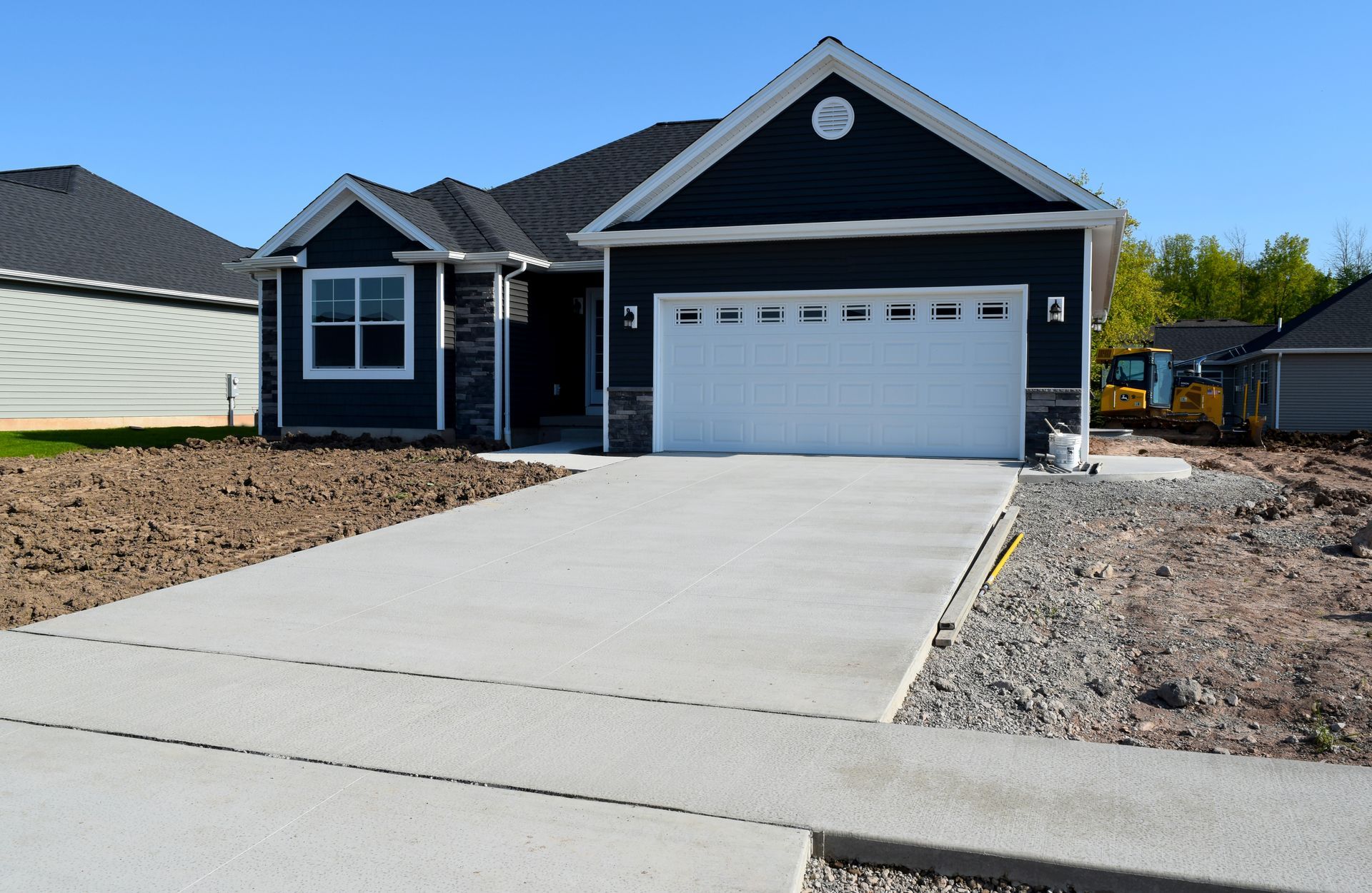 A newly constructed dark navy blue house with a white garage door, concrete driveway, and unfinished landscaping.