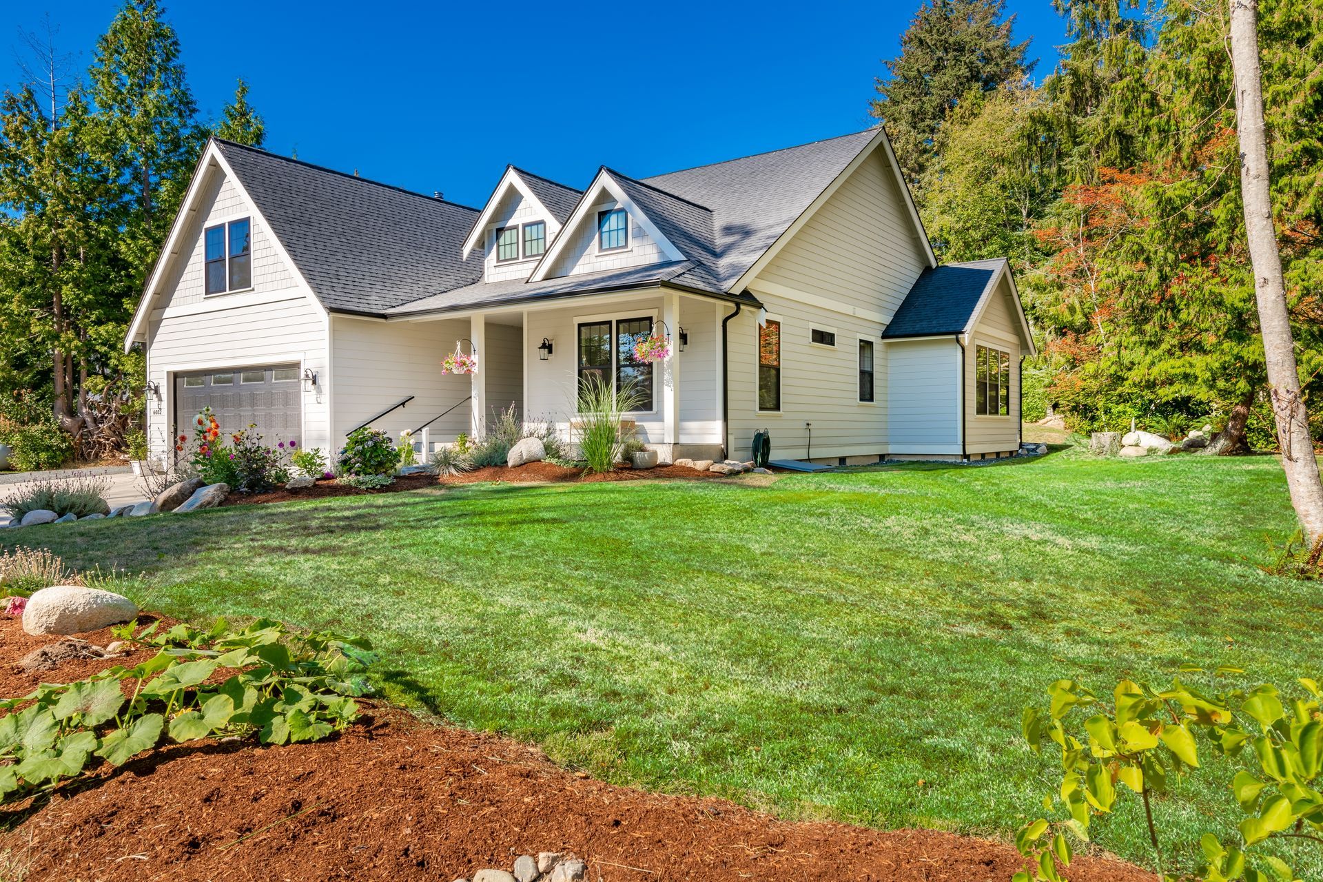 White farmhouse with black trim and gray roof on green lawn.