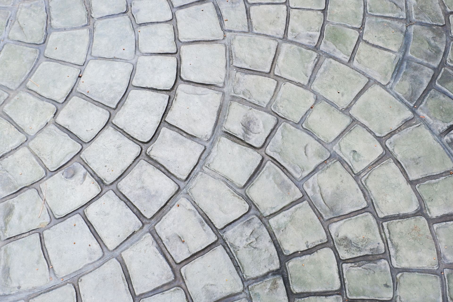 A close-up view of light-gray, textured pavers arranged in a repeating, curved fan pattern.