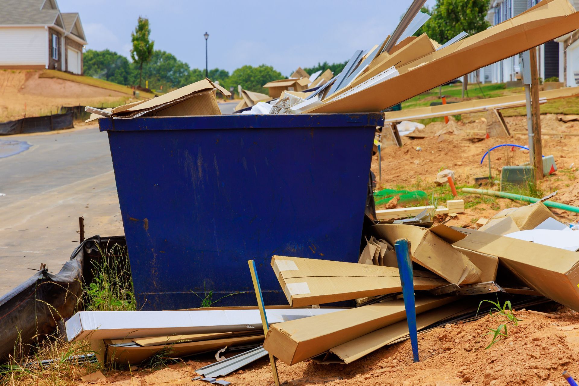A blue construction dumpster overflowing with cardboard and debris at a residential construction site.