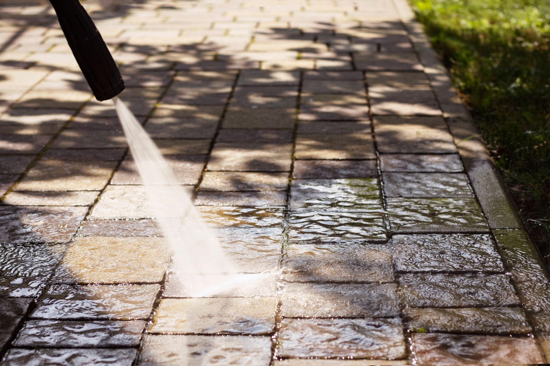 Pressure washer cleaning a brick patio, leaving clean, wet path.