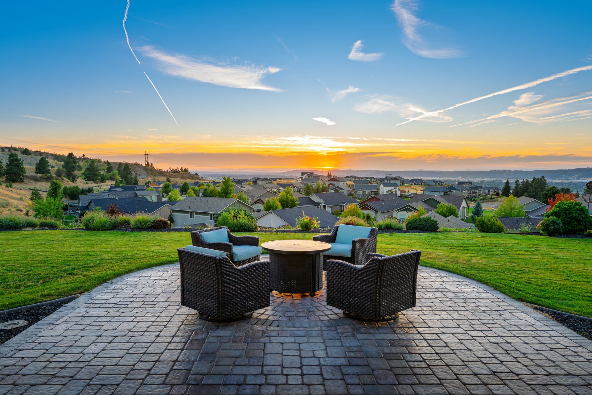 Four chairs and a fire pit on a stone patio overlooking a residential neighborhood at sunset.