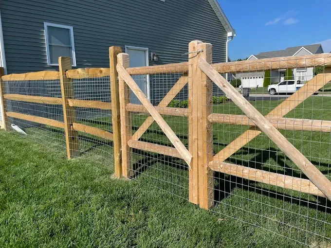 Wooden fence with gate; attached wire mesh. Green grass, blue house exterior.