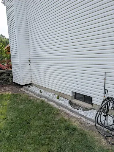 White house siding with a small rock bed along the foundation, green grass in front.