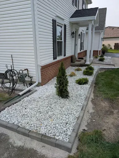 White house with rock garden, shrubs, and a paved border.