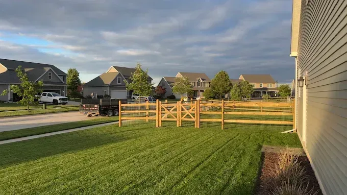 Lawn and a split-rail fence in front of several houses under a partly cloudy sky.